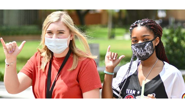Two female students wearing masks showing the Maverick hand sign.